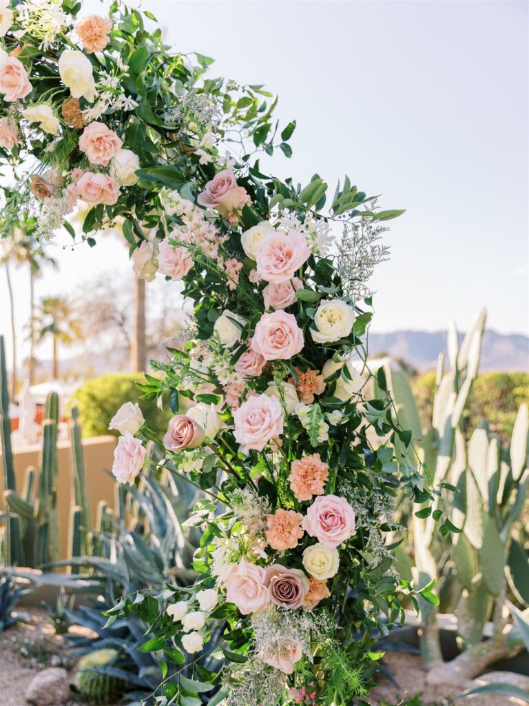 Close up of wedding ceremony arch made of greenery and white, blush, mauve, and pink flowers.