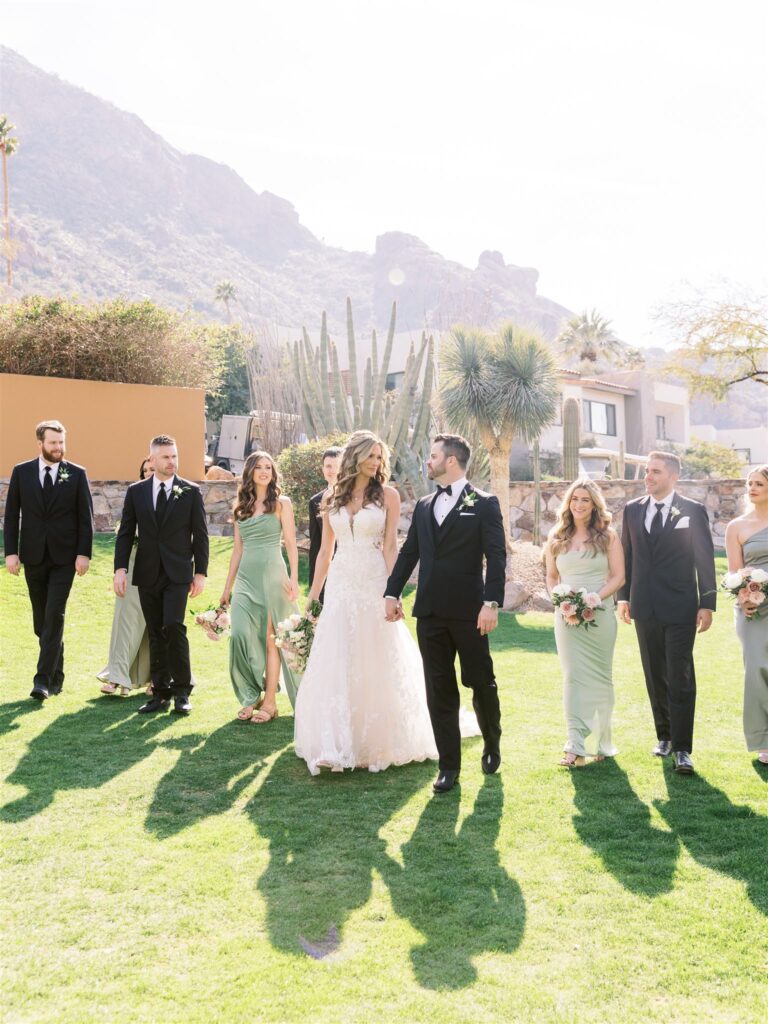 Bride and groom walking in a line with wedding party on grass with bridesmaids in mint green shades and men in black suits.