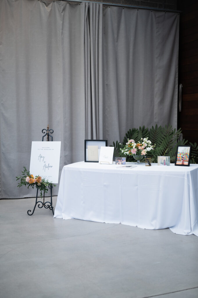 Welcome table with floral arrangement and guestbook at indoor space with welcome sign next to it.