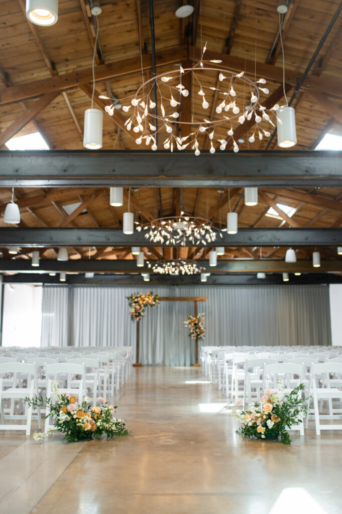 Set wedding ceremony space at The Clayton House with arch in altar space and back of aisle ground floral arrangements.