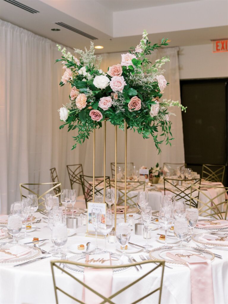 Tall reception centerpiece on gold stand and floral design of greenery with white, pink, and mauve floral.