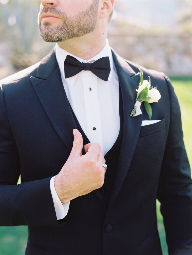 Groom in black suit with boutonniere of white flowers and greenery.