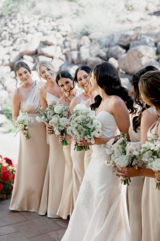 Bride with bridesmaids in taupe gowns, all smiling, holding bouquts.