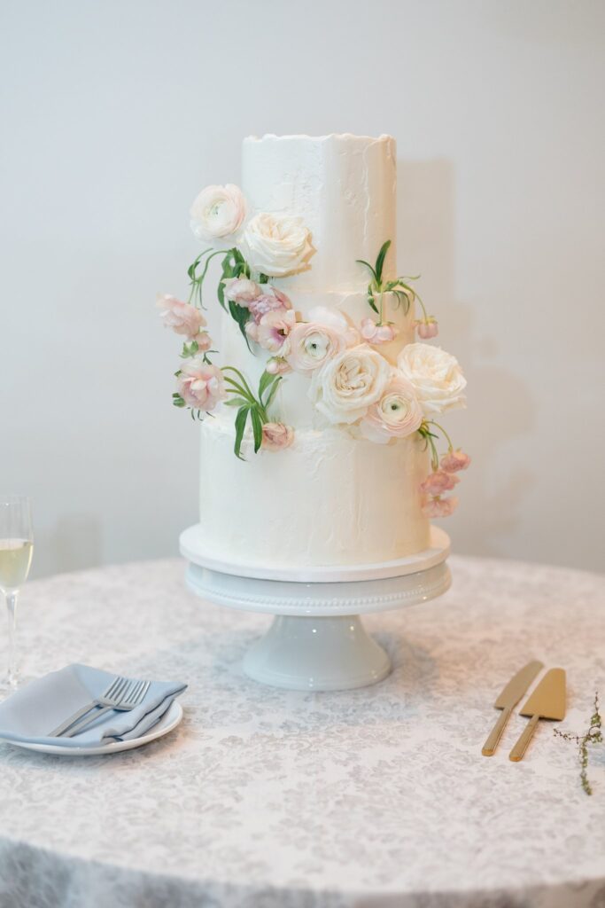 White three tiered wedding cake with white and blush floral and greenery added to it.