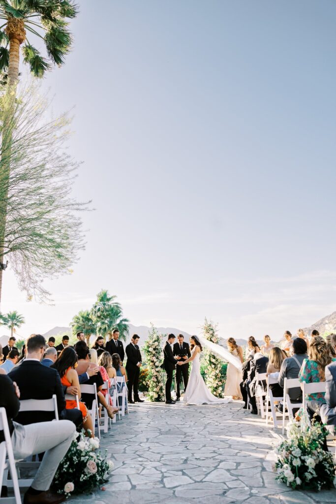 Bride and groom at altar space during outdoor wedding ceremony at Sanctuary Resort with floral pillars framing them and aisle gound floral arrangements.