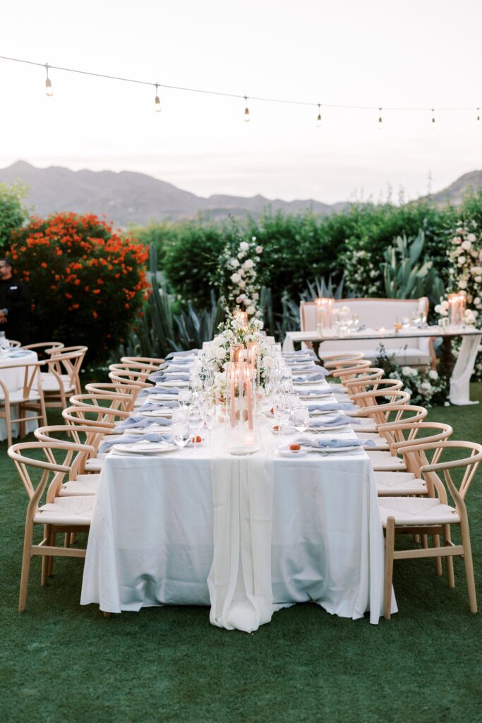 Long outdoor reception table settings with candles and floral centerpieces.
