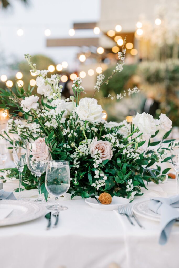 Lush greenery and white and blush floral centerpiece on wedding reception table.