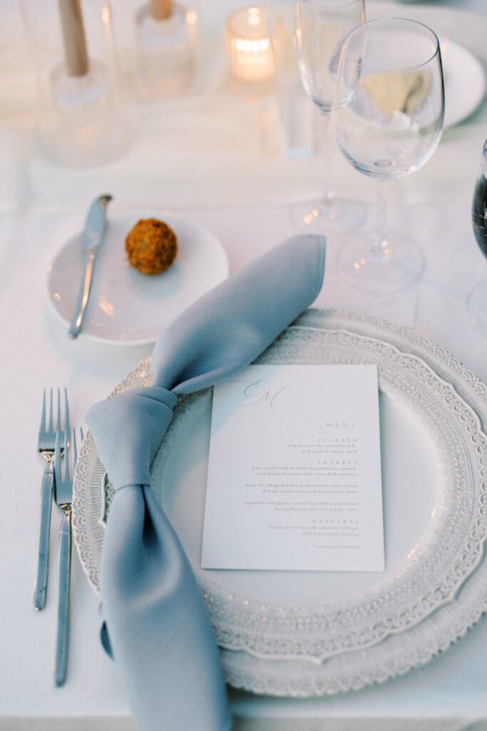 Wedding place setting with detailed white plates and blue napkin.