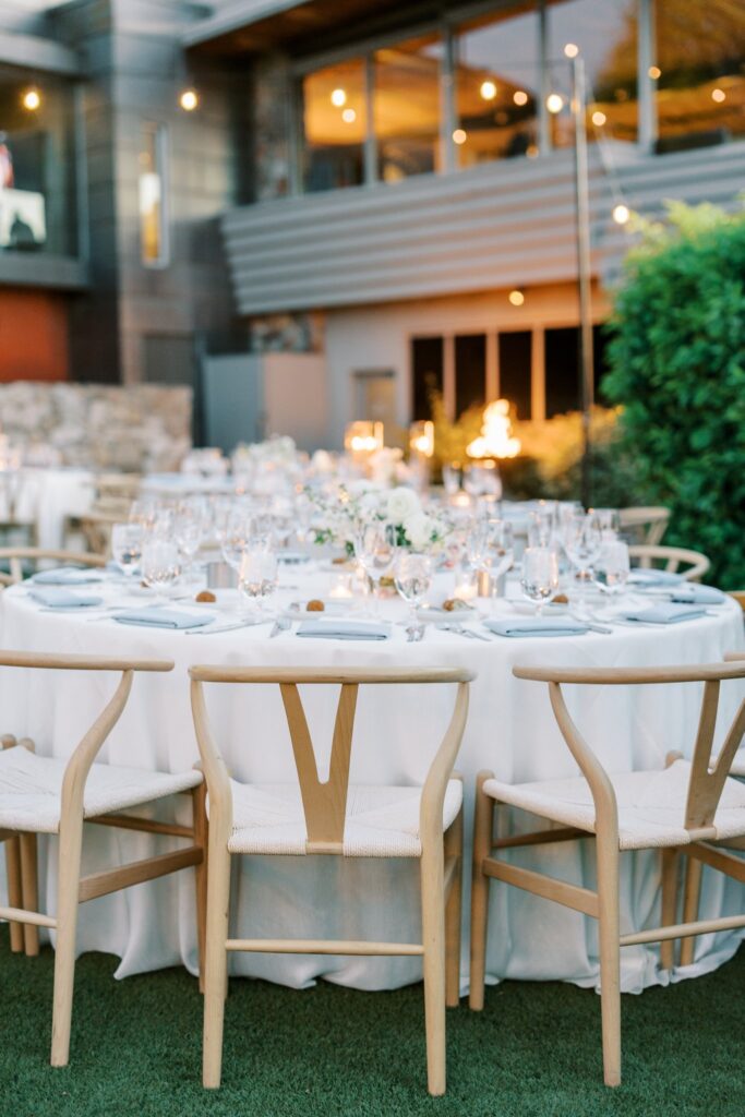 Round outdoor reception table settings with candles and floral centerpieces.