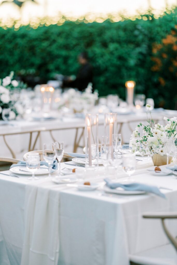 Outdoor reception table settings with candles and floral centerpieces.