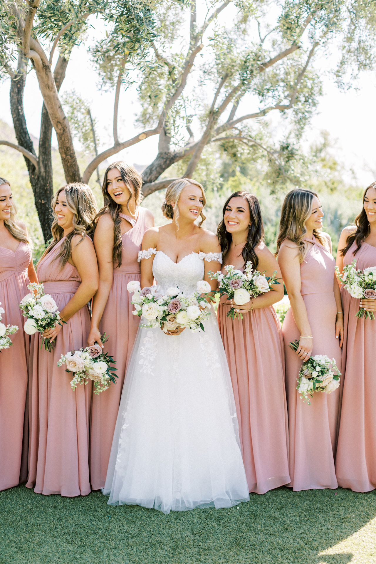 Bride standing in row with bridesmaids wearing blush bridesmaid dresses, all smiling.