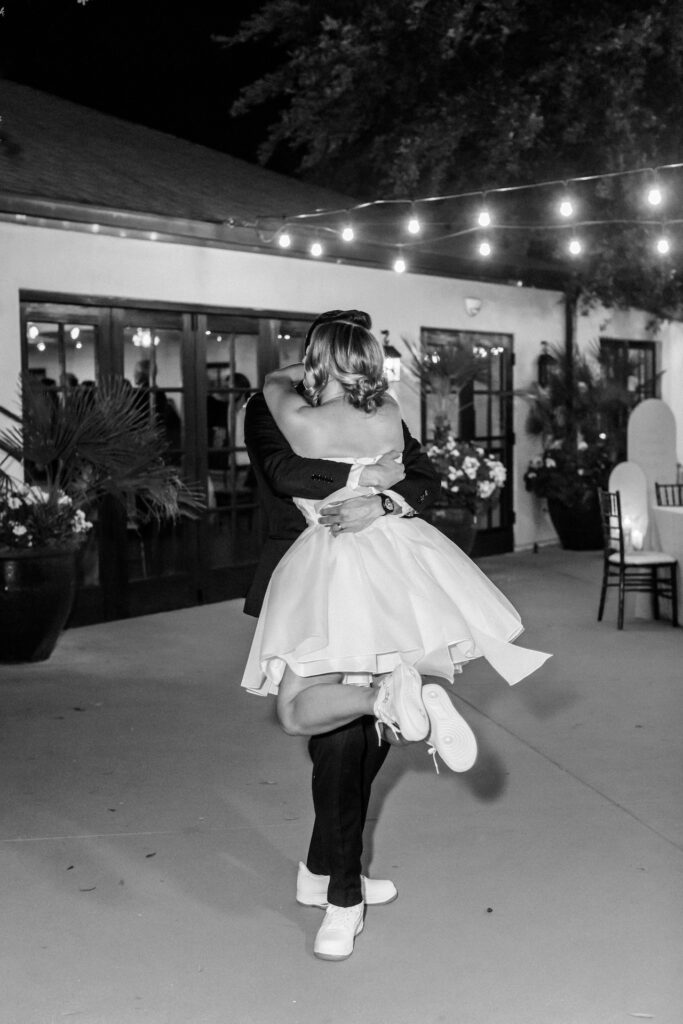 Groom holding bride up around waist, embracing at wedding reception.