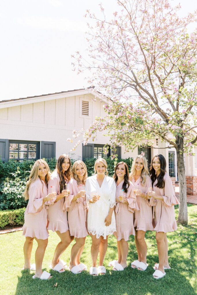 Bride standing in a row with bridesmaids in blush bathrobes.