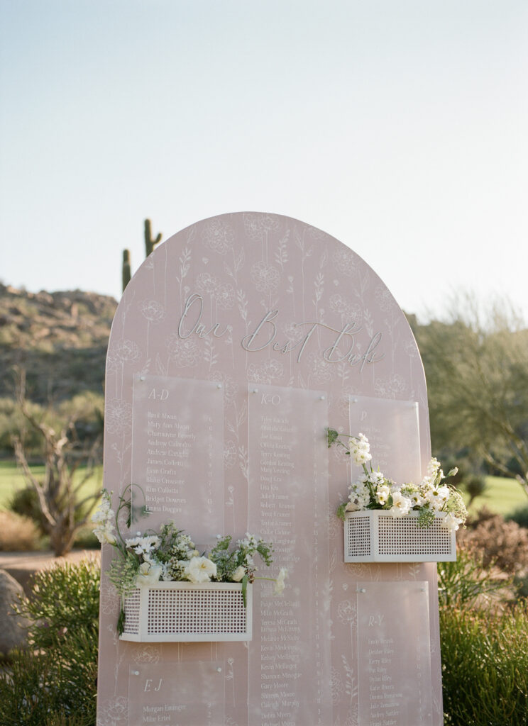Custom wedding escort board of pink with white floral details and with live floral installation.