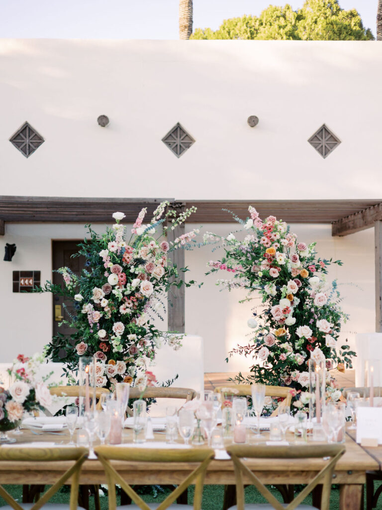 Floral pillars behind long reception table at outdoor celebration.