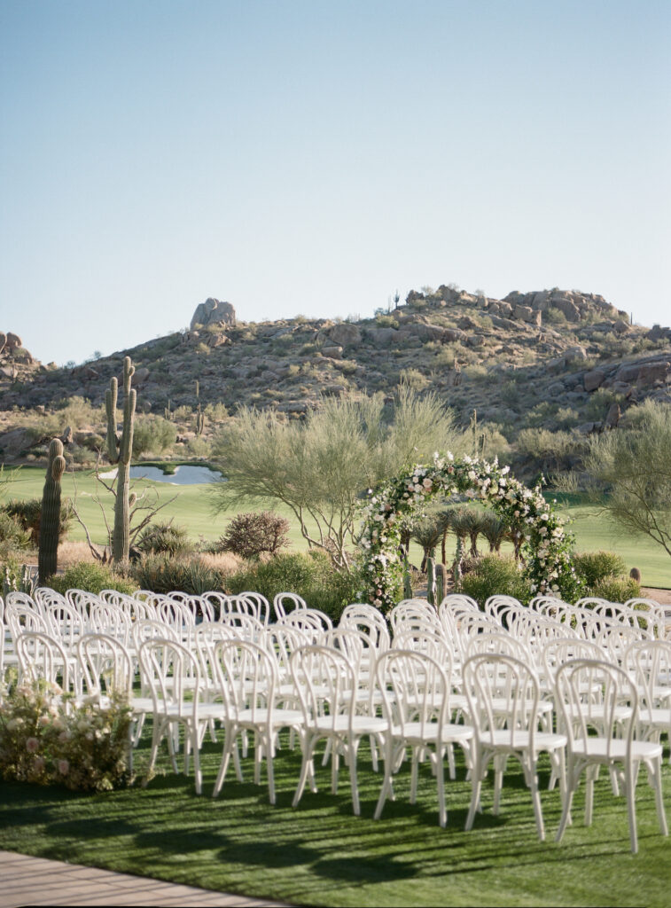 Outdoor wedding ceremony at Estancia with desert scenery and large floral and greenery arch.