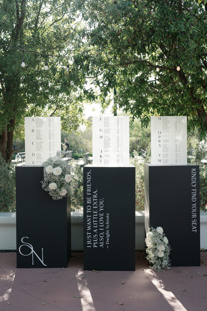 Custom white and black wedding reception escort boards with baby's breath and white roses floral installations.