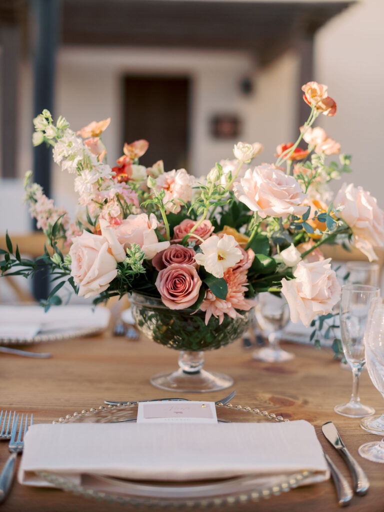 Wedding reception centerpiece in glass vase of white, blush, and peach floral and greenery.