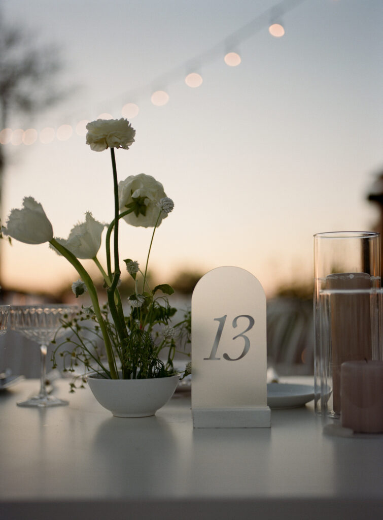 Frosted clear table number next to flower centerpiece in a bowl.