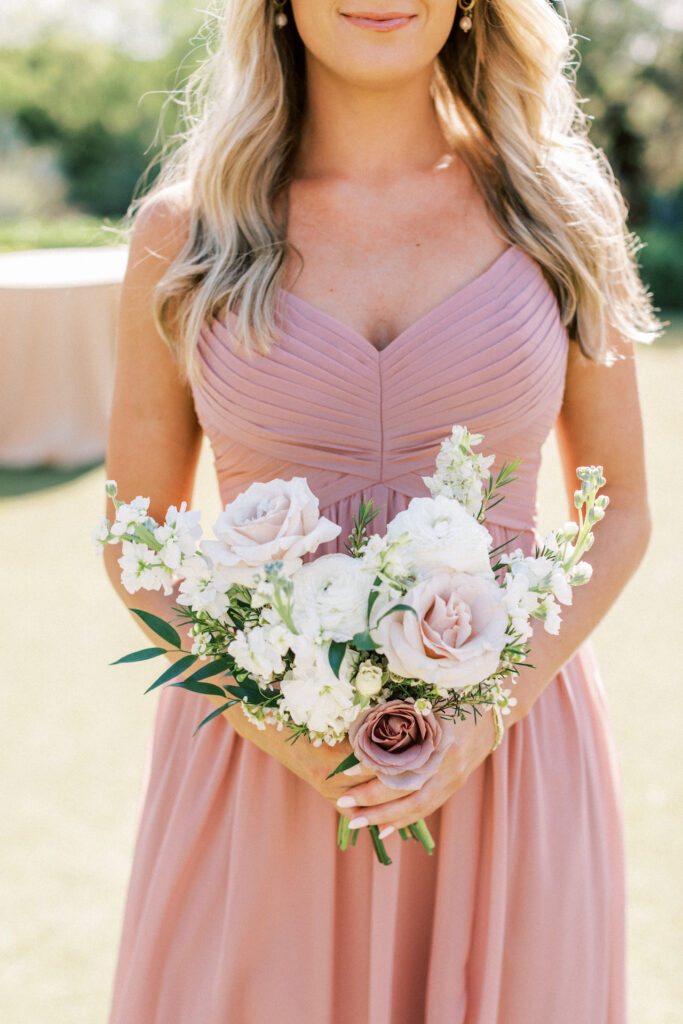Bridesmaid in blush gown holding bouquet of white and blush flowers.