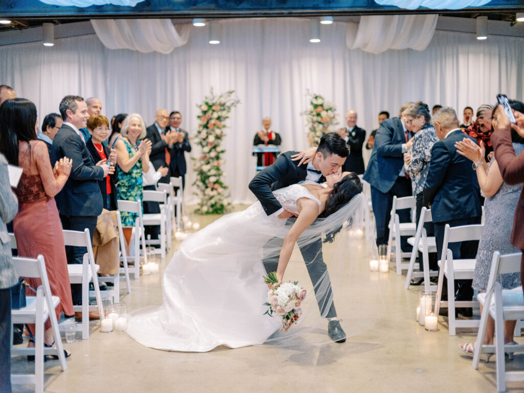 Groom dipping bride and kissing her in middle of indoor wedding ceremony aisle at The Clayton House.