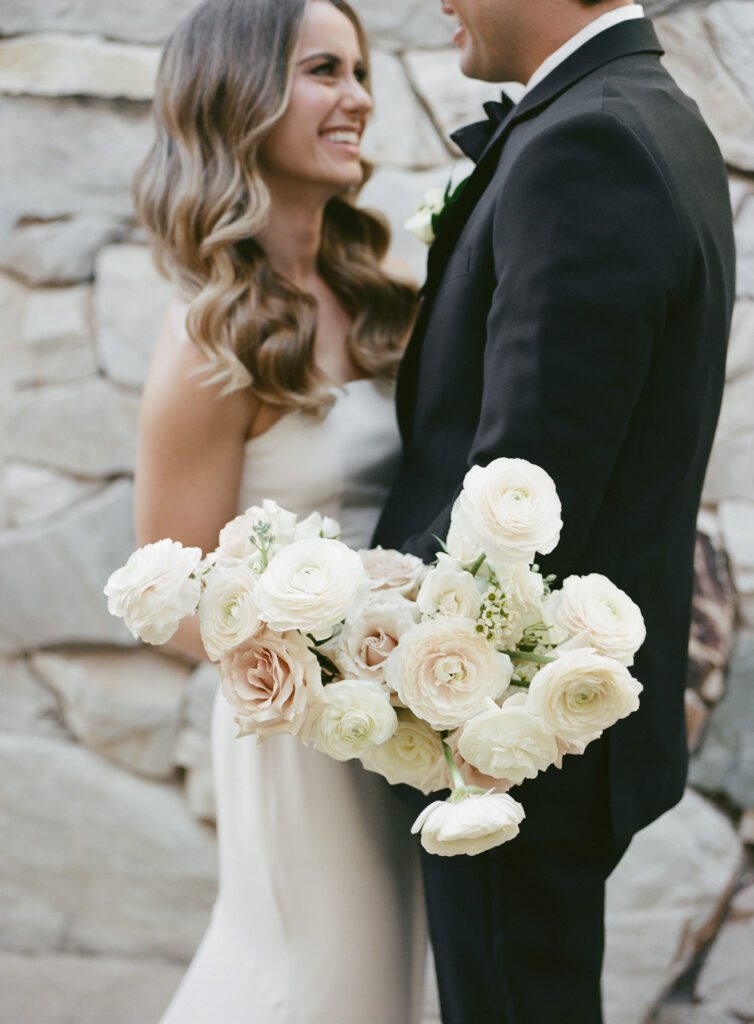 Bride and groom embracing, bride holding white and blush roses bouquet at Estancia.