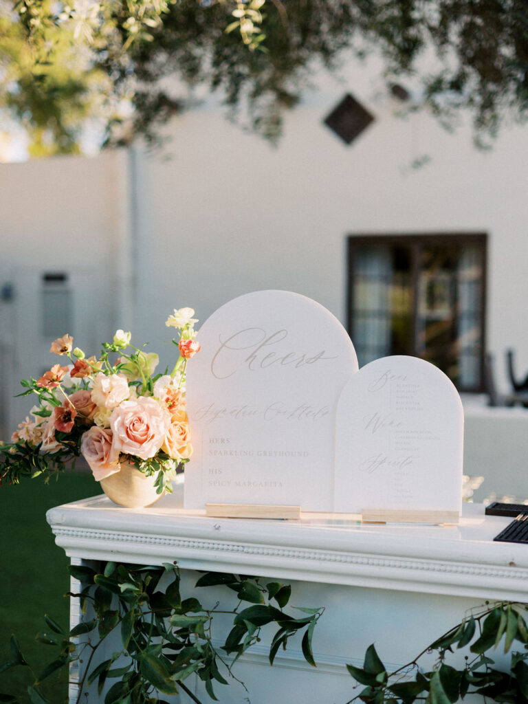 Custom bar top menu signs at wedding reception with a floral arrangement next to them.