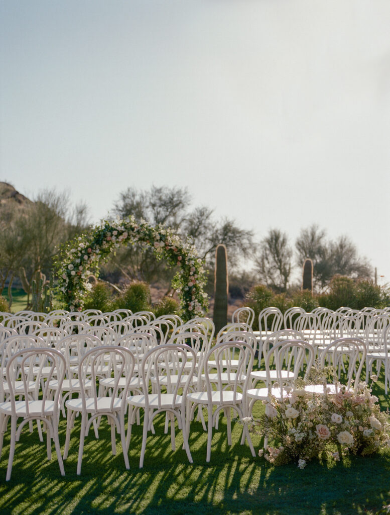 Outdoor wedding ceremony at Estancia with desert scenery and large floral and greenery arch.