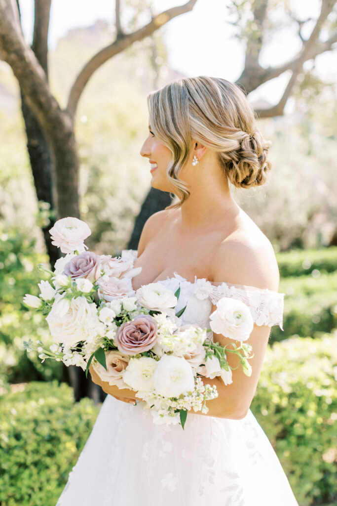 Bride looking off and standing sideways holding bouquet in desert landscape.