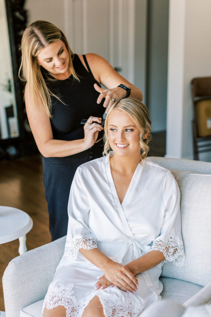 Hairstylist styling bride's hair before wedding.
