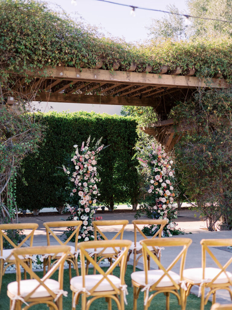Outdoor wedding ceremony at Wigwam with flower pillars of pink, white, peach.
