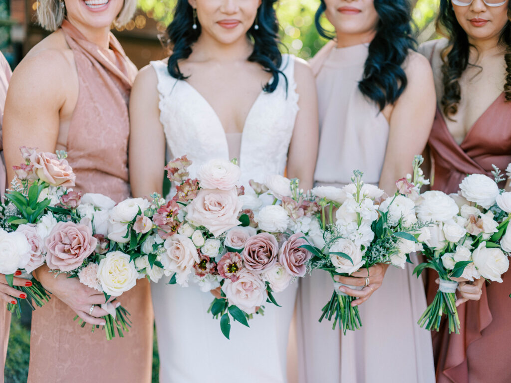 Bride with bridesmaids in pink and mauve gowns holding bouquets of pink and white flowers.