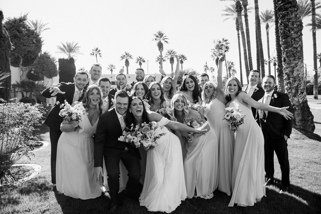 Black and white picture of wedding party outside with bride and groom at center, all smiling.