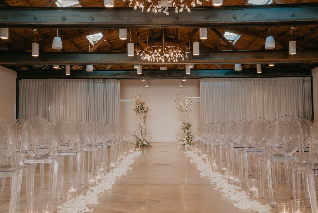 The Clayton House wedding ceremony with aisle rose pedals, candles, clear acrylic chairs, and altar space floral columns with no guests seated.