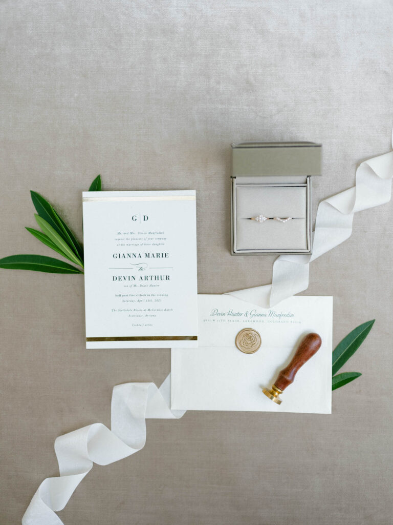 Custom white wedding invitation and envelope with white ribbon, rings and greenery.
