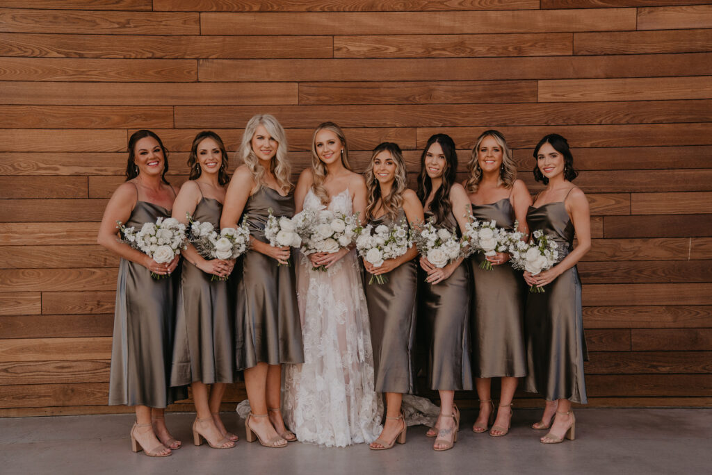 Bride standing with bridesmaids all holding white flower bouquets and brides wearing dark taupe dresses.