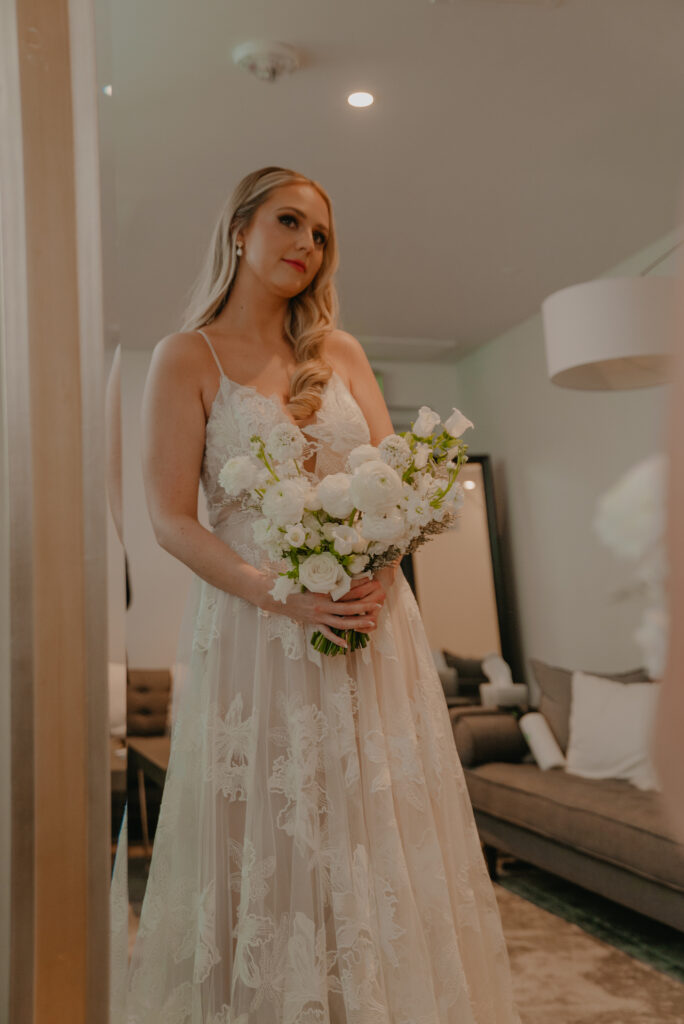 Bride looking into mirror, holding bouquet of white flowers.