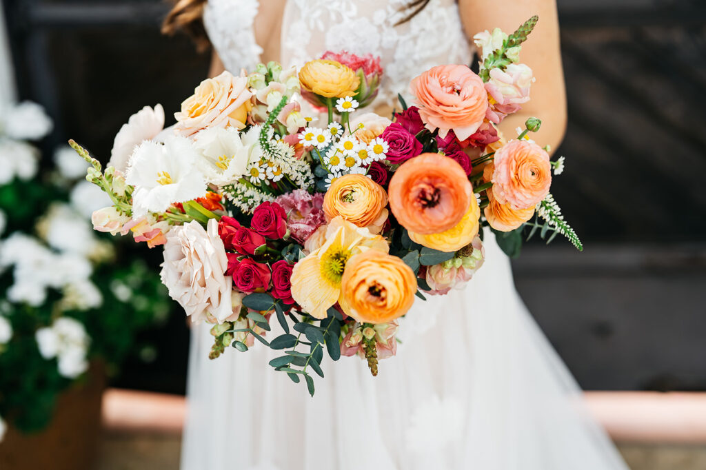 Colorful bridal bouquet of peach, pink, yellow, and white flowers including roses and ranunculus.
