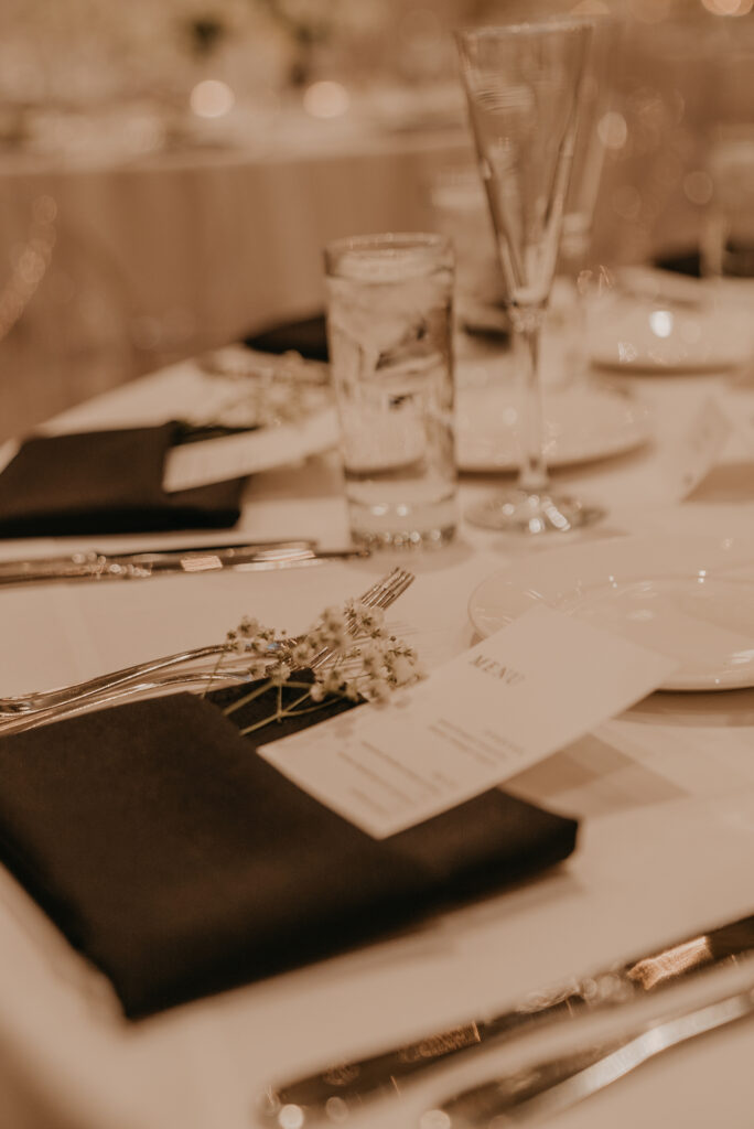 Wedding reception place settings with baby's breath flowers and menu in black napkin.