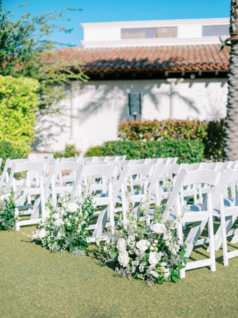 Outdoor wedding ceremony aisle ground arrangements of white floral and greenery.