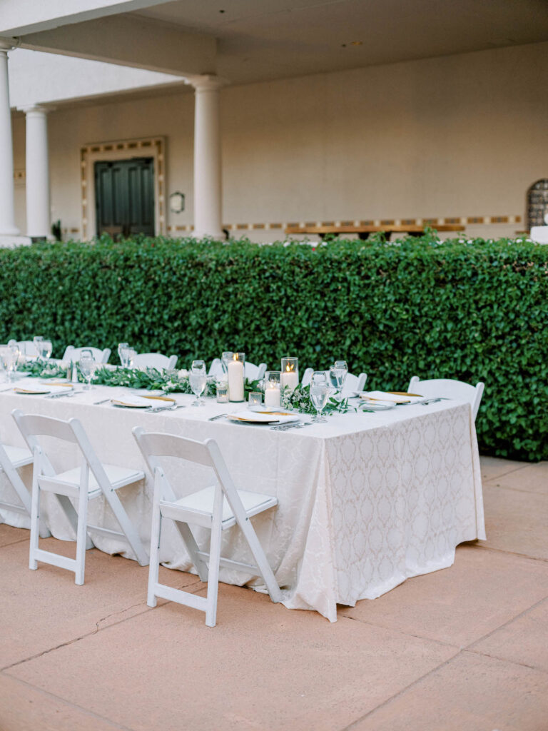 Long table at outdoor wedding reception with greenery and candles down the middle.
