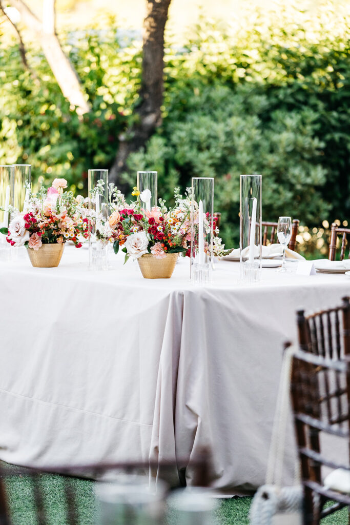 Outdoor reception table with taupe linen and floral arrangements in copper vases and taper candles.