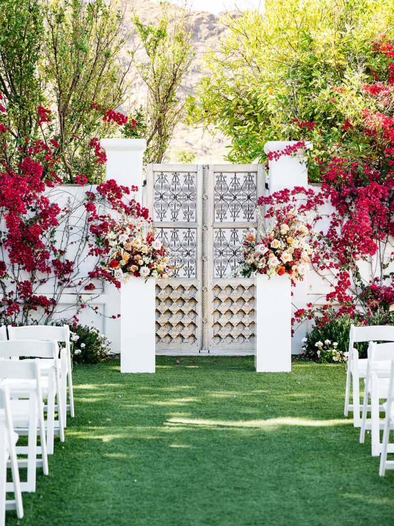 Two large reaching floral arrangement on white acrylic pillar at outdoor wedding ceremony at El Chorro on Herb Garden lawn.