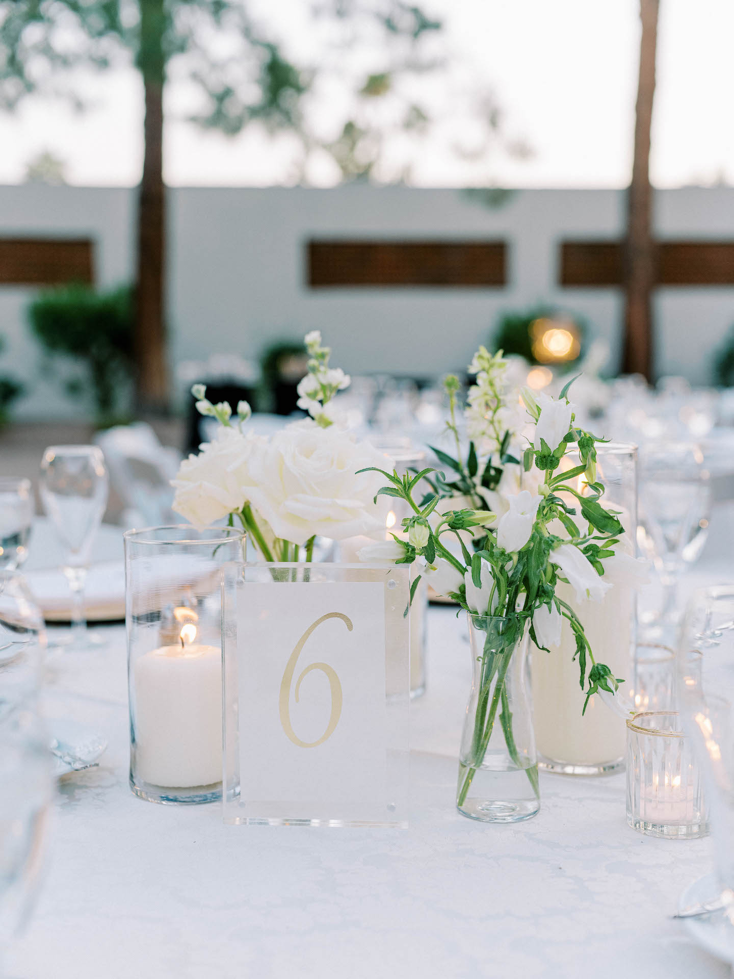 Wedding reception centerpiece of candles and white flowers bud vases and a glass etched table number.