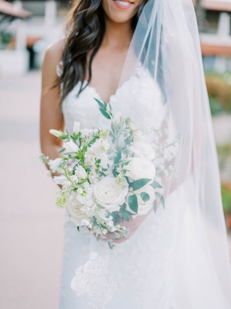 Bride holding bouquet of white flowers and greenery.