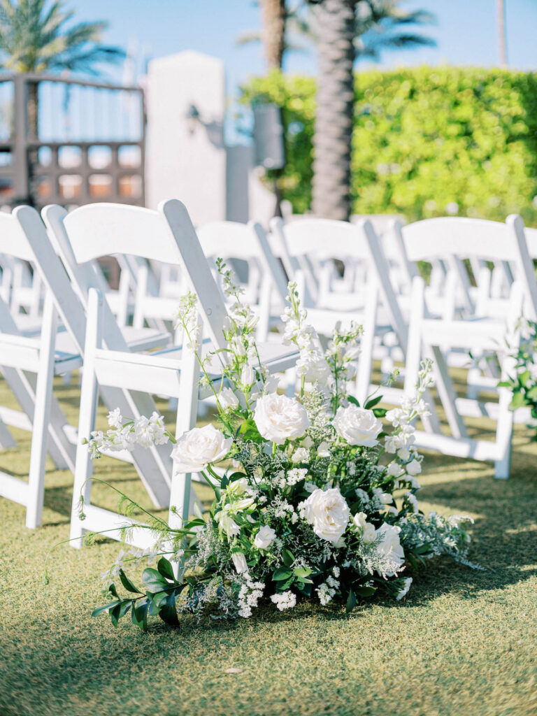 Outdoor wedding ceremony aisle ground arrangement of white floral and greenery.