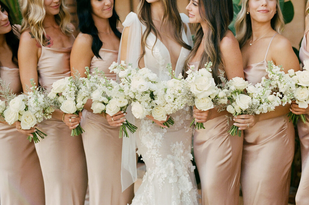 Bride standing with bridesmaids, smiling, all holding white floral bouquets.