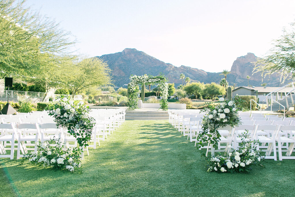Outdoor wedding ceremony space at Mountain Shadows with floral decorated chuppah in altar space and back of aisle arrangements on ground and clear acrylic pillars.