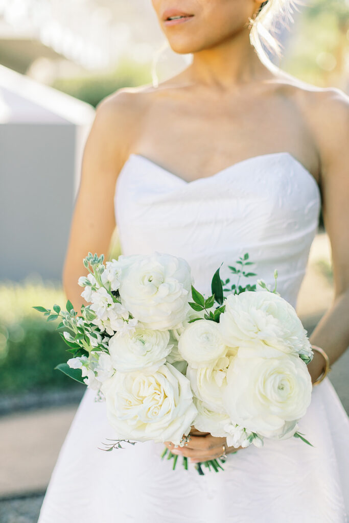 Bride holding white flowers bouquet of ranunculus and roses, snapdragons.