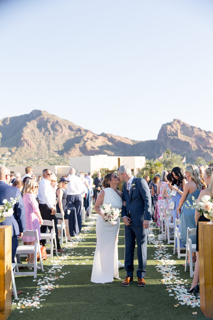 Bride and groom kissing in outdoor wedding ceremony aisle.